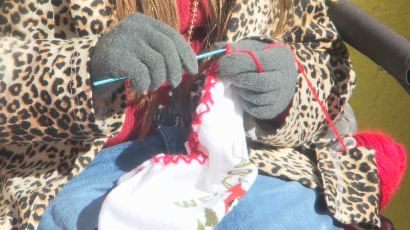 A girl knits a scarf as customers watch and get ready to make a purchase.